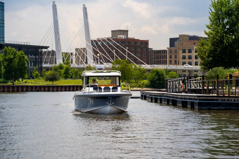  Yacht Photos Pics 2025 Nimbus Commuter 9 boat cruising near urban waterfront with modern bridge in background.