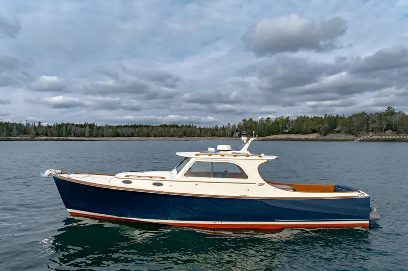 Lab Adore Yacht Photos Pics 2003 Hinckley Picnic Boat EP on calm water, cloudy sky, forested shoreline.