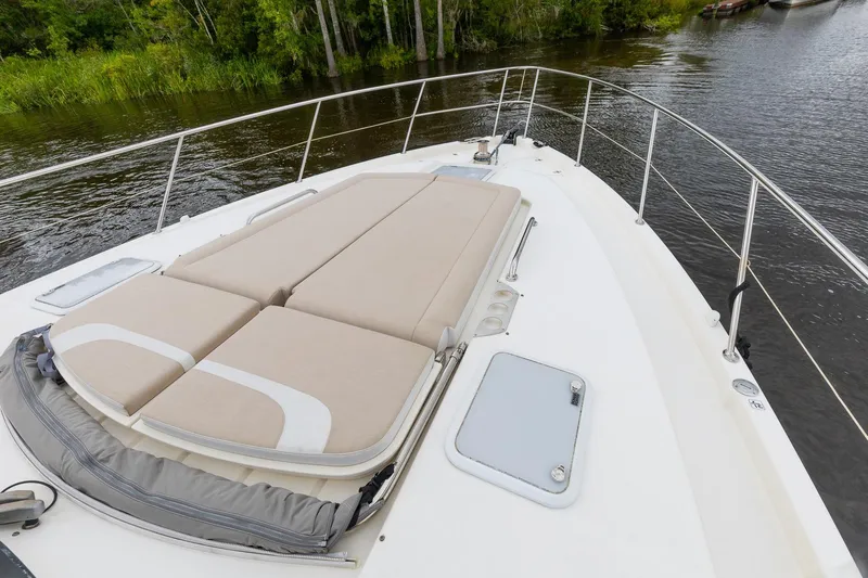 Frivolous Yacht Photos Pics 2021 Riviera 5400 Sport Yacht Platinum Edition with sunbed on deck, near lush greenery.