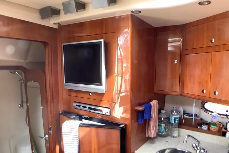 Perseides Yacht Photos Pics 2005 Regal Commodore 3860 yacht interior with TV, wooden cabinets, and kitchenette.