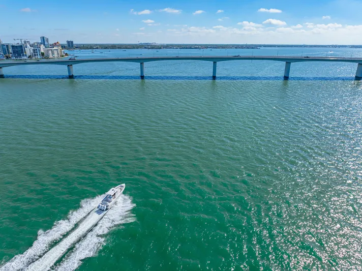 Tt Aloan At Last Yacht Photos Pics 2023 Fountain 32 NX boat cruising under a bridge on a sunny day.