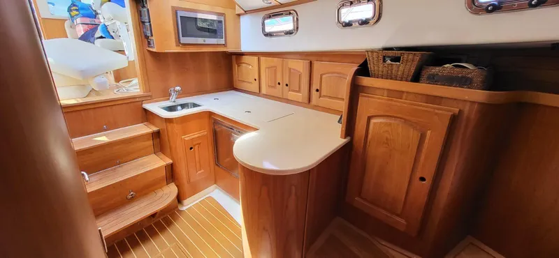  Yacht Photos Pics 2022 Legacy 36 yacht interior with wooden cabinetry, compact kitchen, and steps leading to helm.