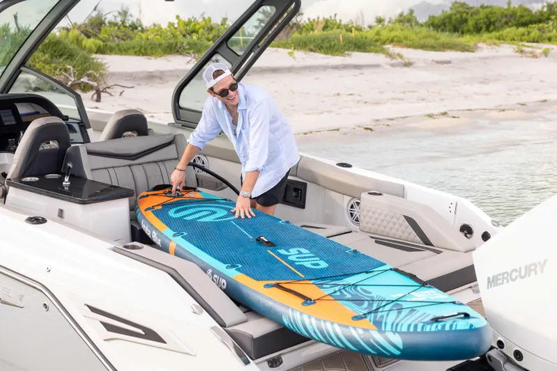  Yacht Photos Pics Person loading paddleboard onto 2026 Monterey ELITE 30 boat at beach.
