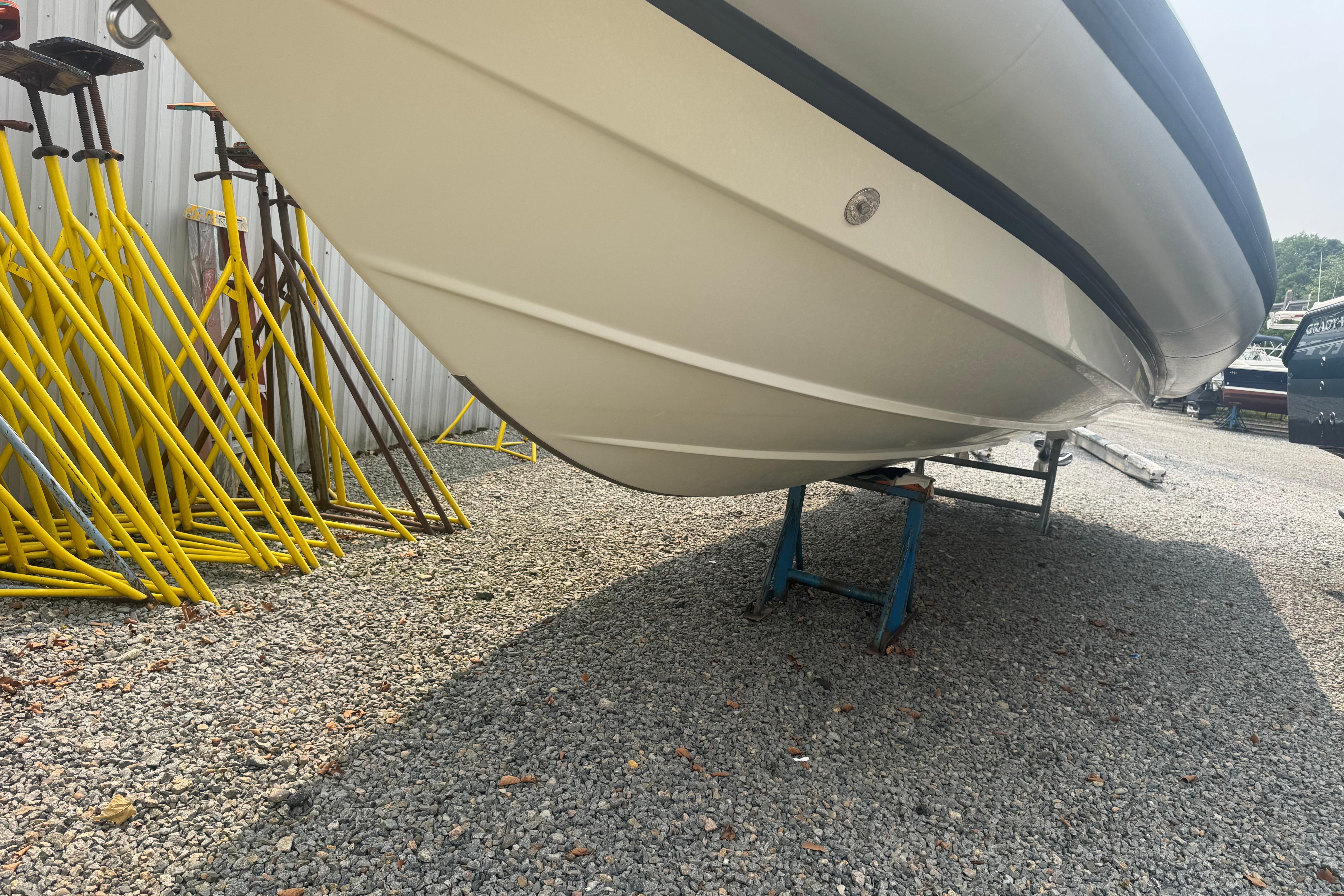 2016 Protector 30 Center Console boat on stands, gravel lot, yellow supports nearby.