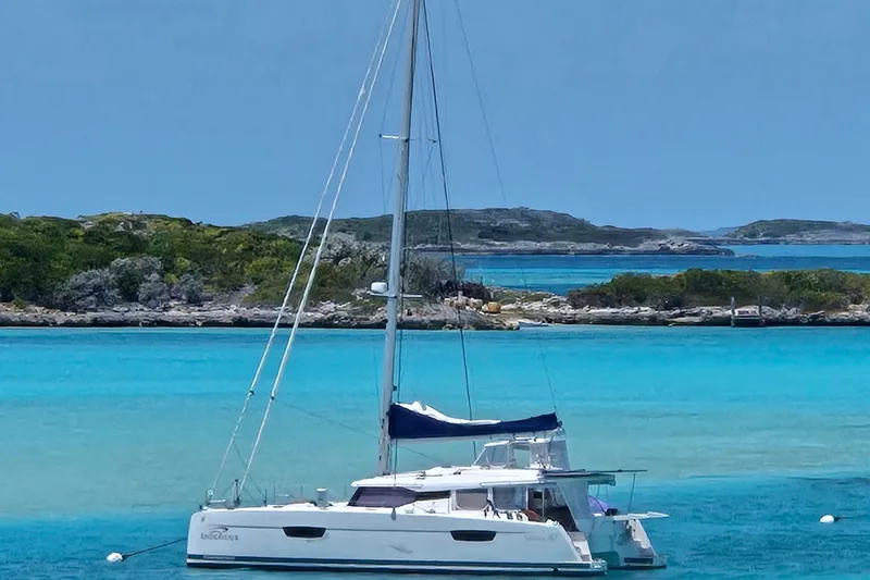 Endeavour Yacht Photos Pics 2020 Fountaine Pajot Saona 47 catamaran anchored in turquoise waters, scenic island backdrop.