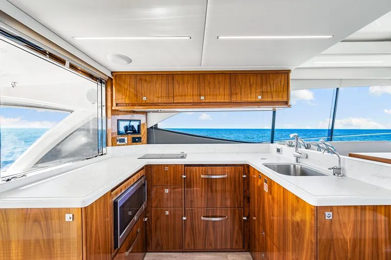  Yacht Photos Pics Luxurious 2022 Riviera 505 SUV yacht kitchen with ocean view, featuring sleek wood cabinetry and modern appliances.