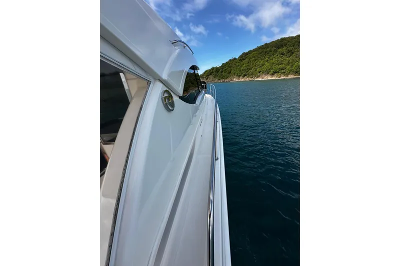  Yacht Photos Pics 2020 Riviera 395 SUV cruising near lush green coastline under blue sky.