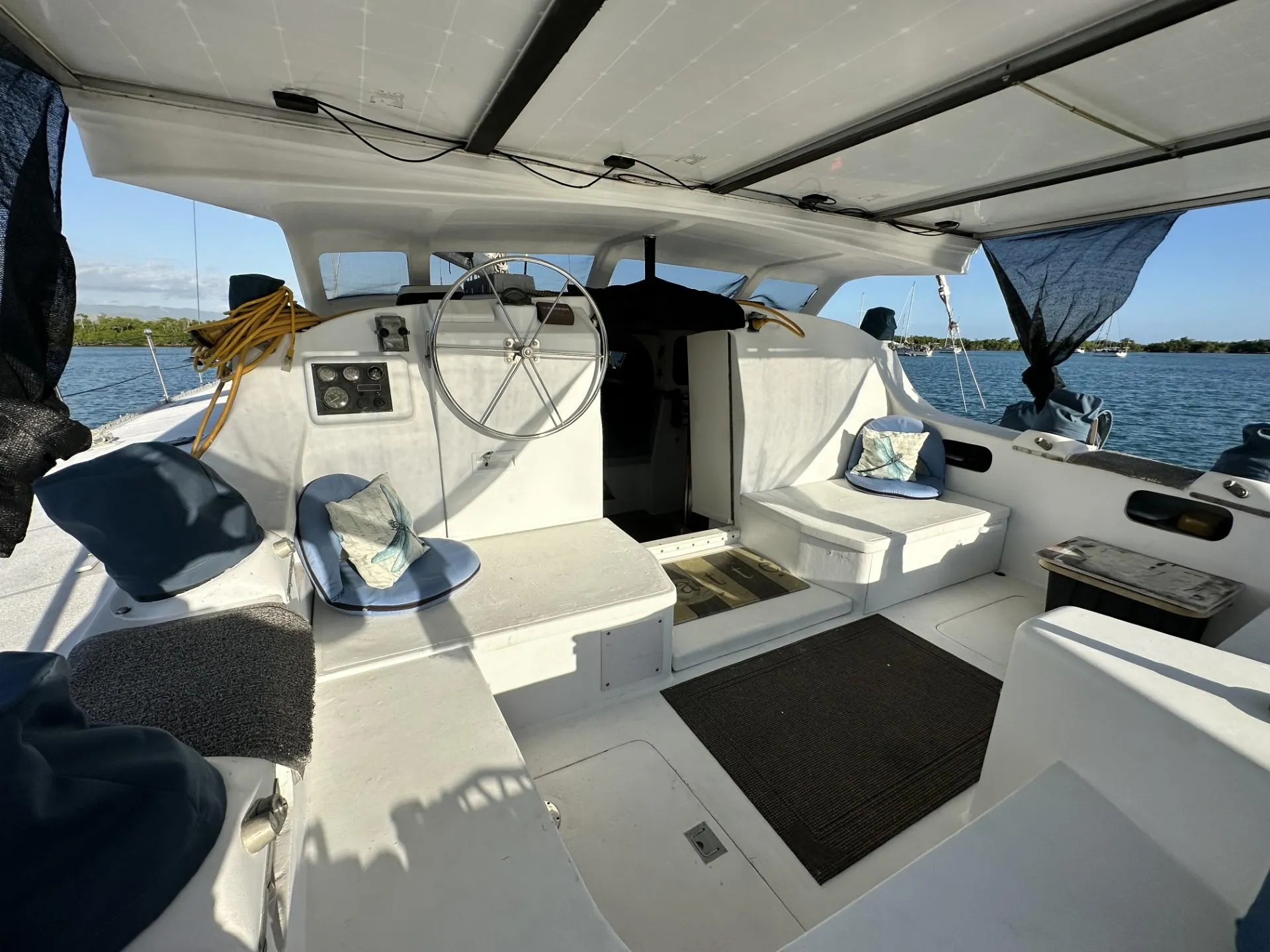 Interior of a 1972 Custom 53 Catamaran with seating and steering wheel, overlooking the water.