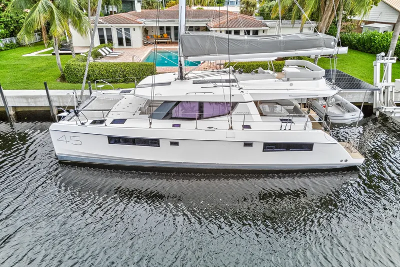 Sundecker Yacht Photos Pics 2021 Leopard 45 catamaran docked by a waterfront home with a pool and lush greenery.