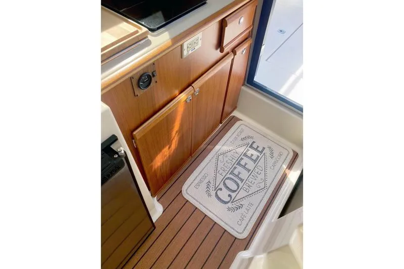  Yacht Photos Pics 2021 Ranger Tugs R-25 interior with wooden cabinetry and a coffee-themed mat.
