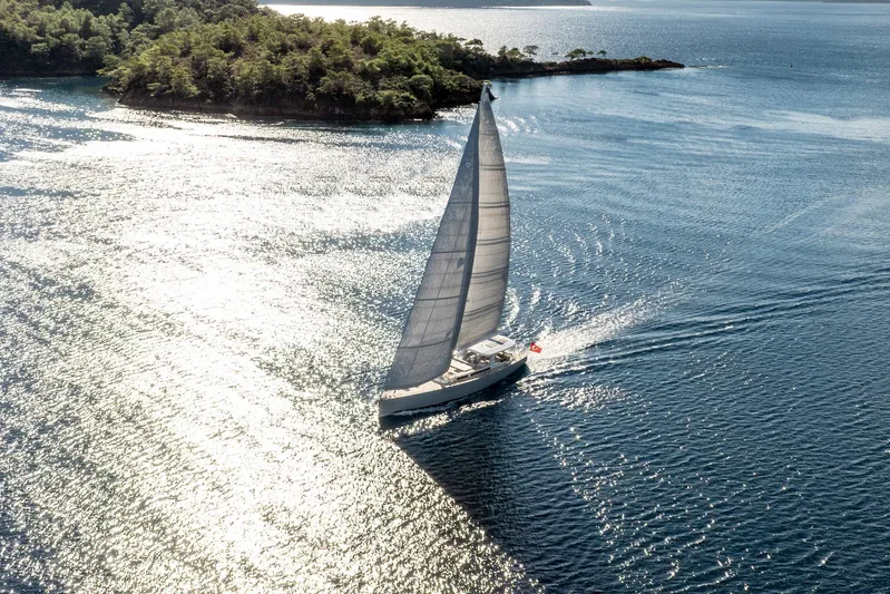 Mishi Yacht Photos Pics Sailboat "Mishi 88" gliding on sunlit water near lush island, 2018 model.