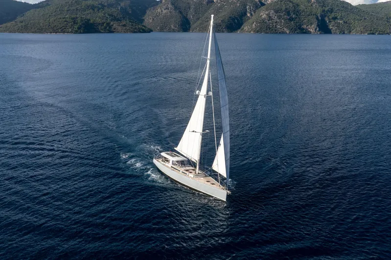 Mishi Yacht Photos Pics Sailing yacht "Mishi 88" gliding on serene waters, surrounded by lush green hills.