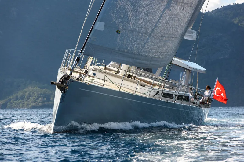 Mishi Yacht Photos Pics Sailing yacht "Mishi 88" gliding on water, Turkish flag, mountainous backdrop.
