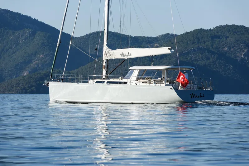 Mishi Yacht Photos Pics Sailing yacht "Mishi 88" on calm waters, mountainous backdrop, Turkish flag displayed.
