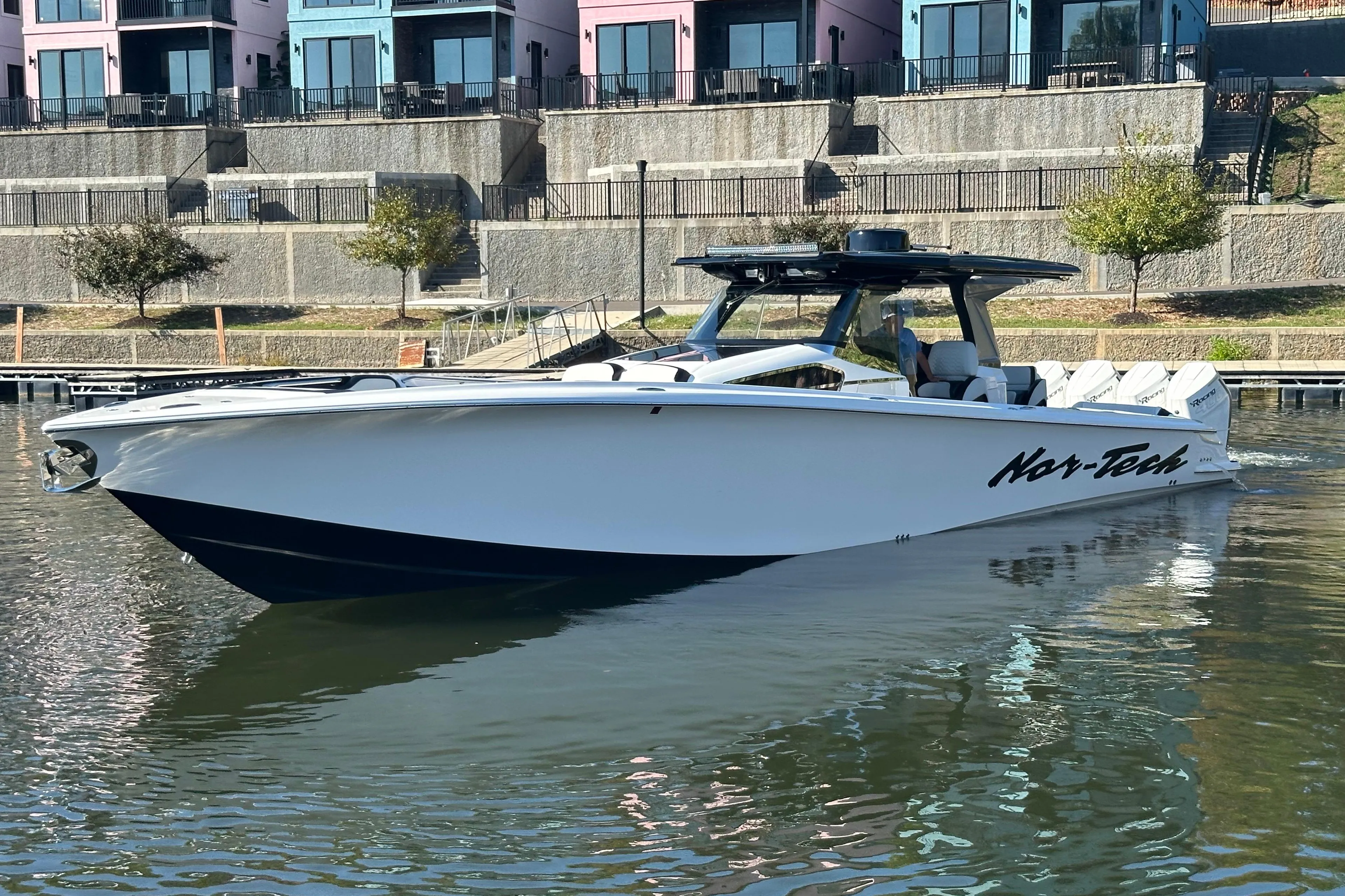 2025 Nor-Tech 450 Sport Center Console boat on calm water near colorful buildings.