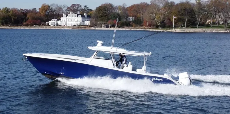  Yacht Photos Pics 2023 Yellowfin 42 Offshore boat cruising on a scenic lake with a mansion in the background.