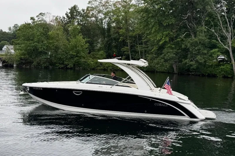  Yacht Photos Pics 2021 Cobalt R30 boat cruising on a serene lake with lush green trees.