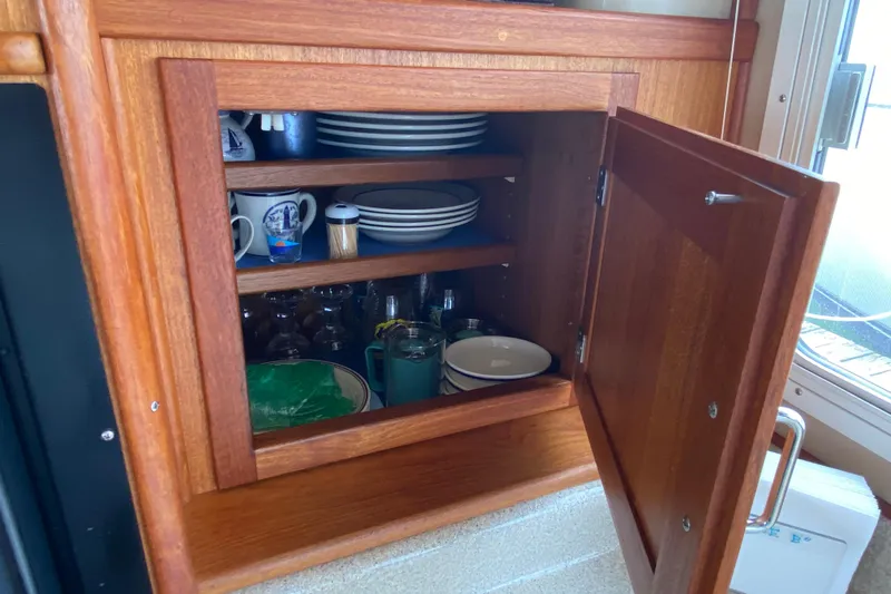 Emilie B Yacht Photos Pics Wooden cabinet with dishes and mugs inside, located on a 2003 American Tug 34 boat.