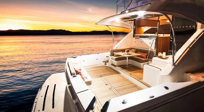  Yacht Photos Pics 2023 Riviera 57 Enclosed Flybridge yacht at sunset, featuring luxurious deck seating.