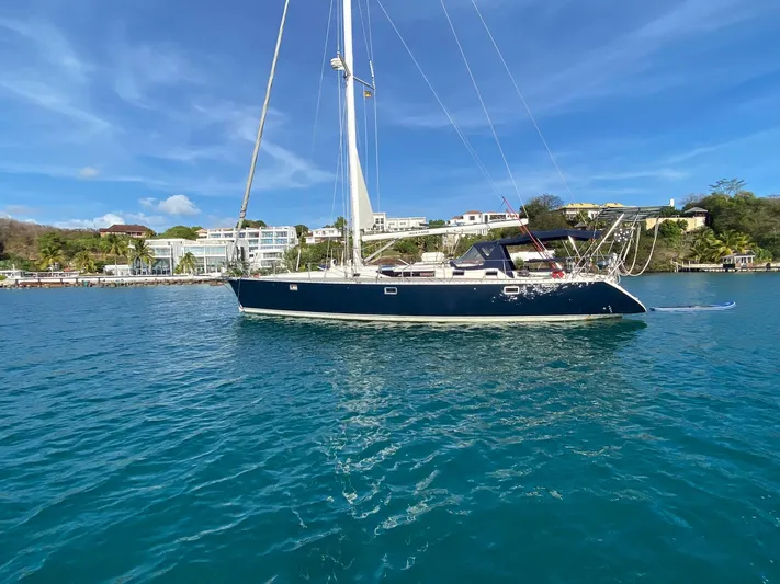 Roxanne Yacht Photos Pics Sailing yacht Beneteau Oceanis Clipper 500, 1990, on clear blue water near a coastal town.