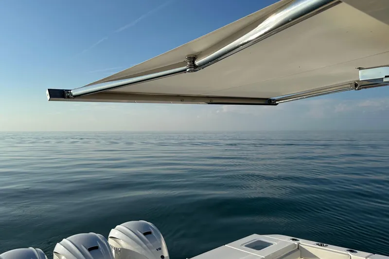  Yacht Photos Pics 2024 Pursuit OS 445 Offshore boat with awning, calm sea, and clear sky.