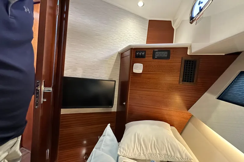  Yacht Photos Pics 2024 Pursuit OS 445 Offshore cabin interior with bed, TV, and wood paneling.
