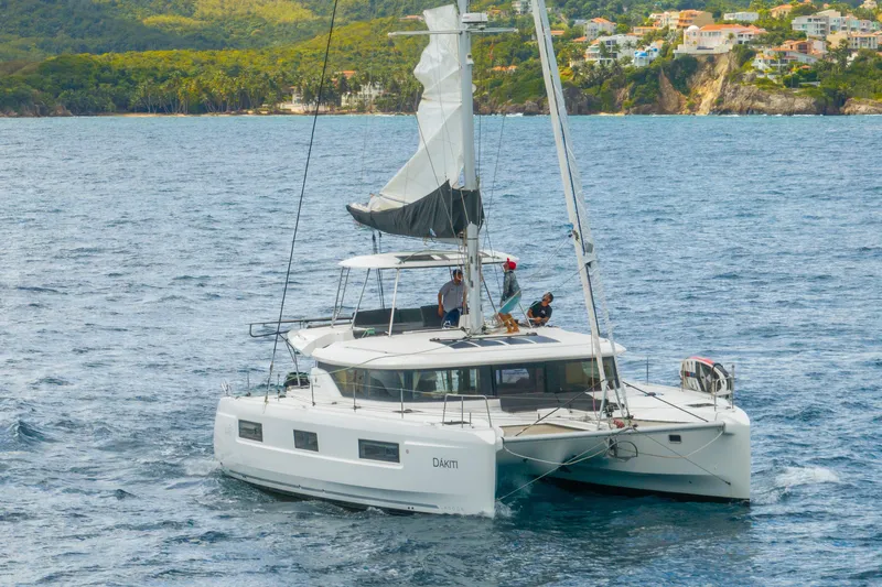 Dakiti Yacht Photos Pics 2023 Lagoon 46 catamaran sailing near a scenic coastline with lush greenery and houses.
