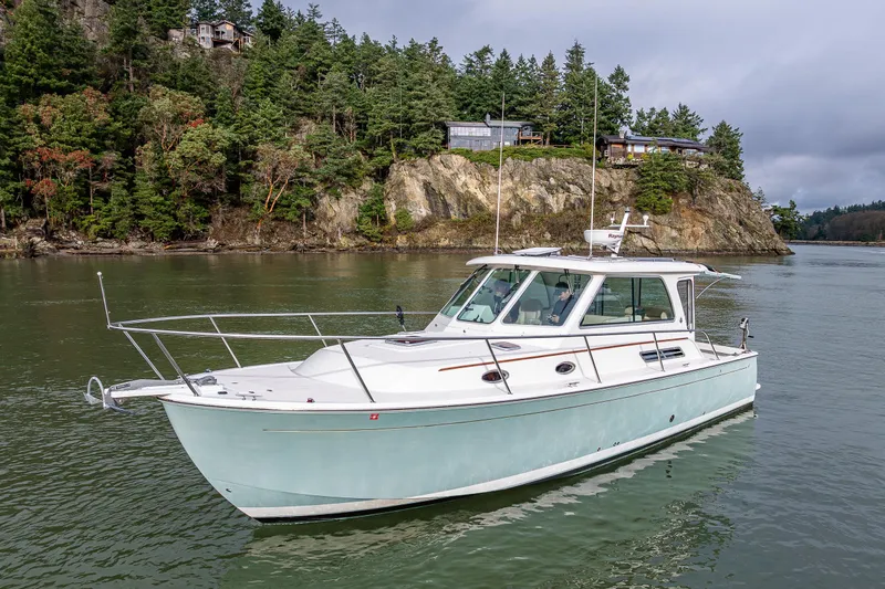Ha Kin Yacht Photos Pics 2008 Back Cove 33 boat cruising near rocky shoreline with lush trees.