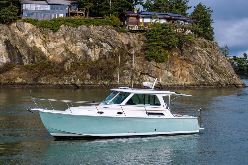 Ha Kin Yacht Photos Pics 2008 Back Cove 33 boat cruising near rocky shoreline with houses above.