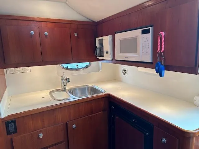  Yacht Photos Pics 2000 Tiara Yachts 3700 Open kitchen with wood cabinets, sink, microwave, and porthole.