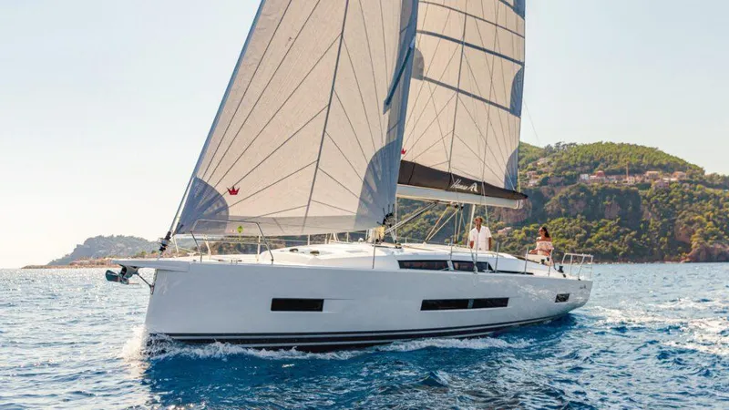  Yacht Photos Pics 2025 Hanse 410 yacht sailing on clear blue waters near a scenic coastline.