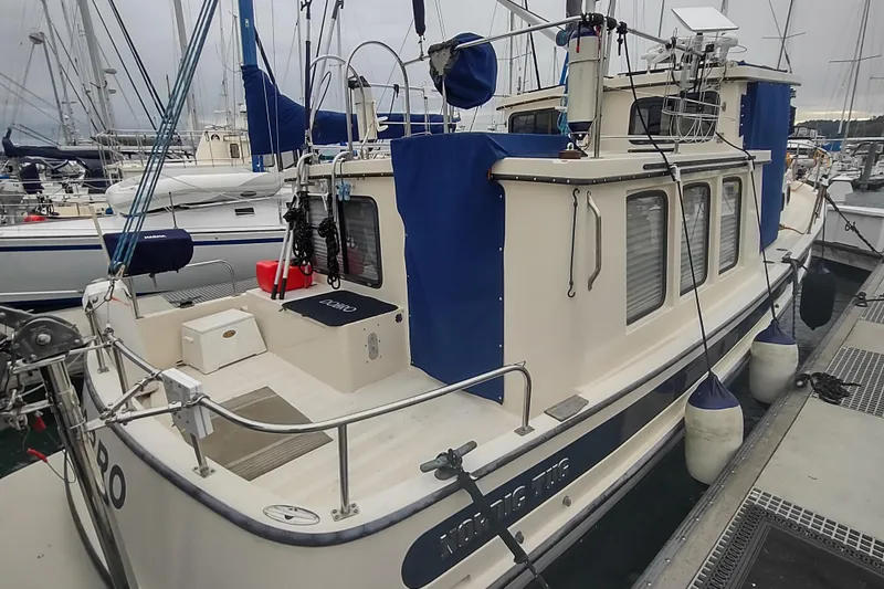 Dobro Yacht Photos Pics 1990 Nordic Tug 32 docked at marina, featuring blue covers and fenders.