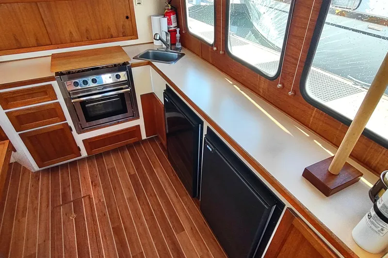 Dobro Yacht Photos Pics 1990 Nordic Tug 32 interior kitchen with wood cabinetry, stove, sink, and windows.