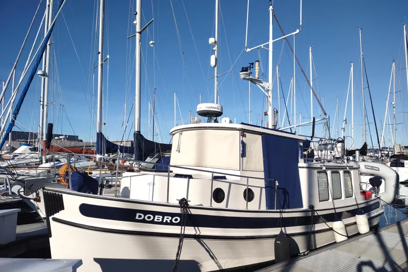 Dobro Yacht Photos Pics 1990 Nordic Tug 32 docked at marina, surrounded by sailboats under clear blue sky.
