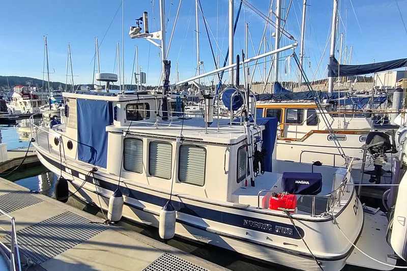 Dobro Yacht Photos Pics 1990 Nordic Tug 32 docked at marina, surrounded by sailboats under clear blue sky.