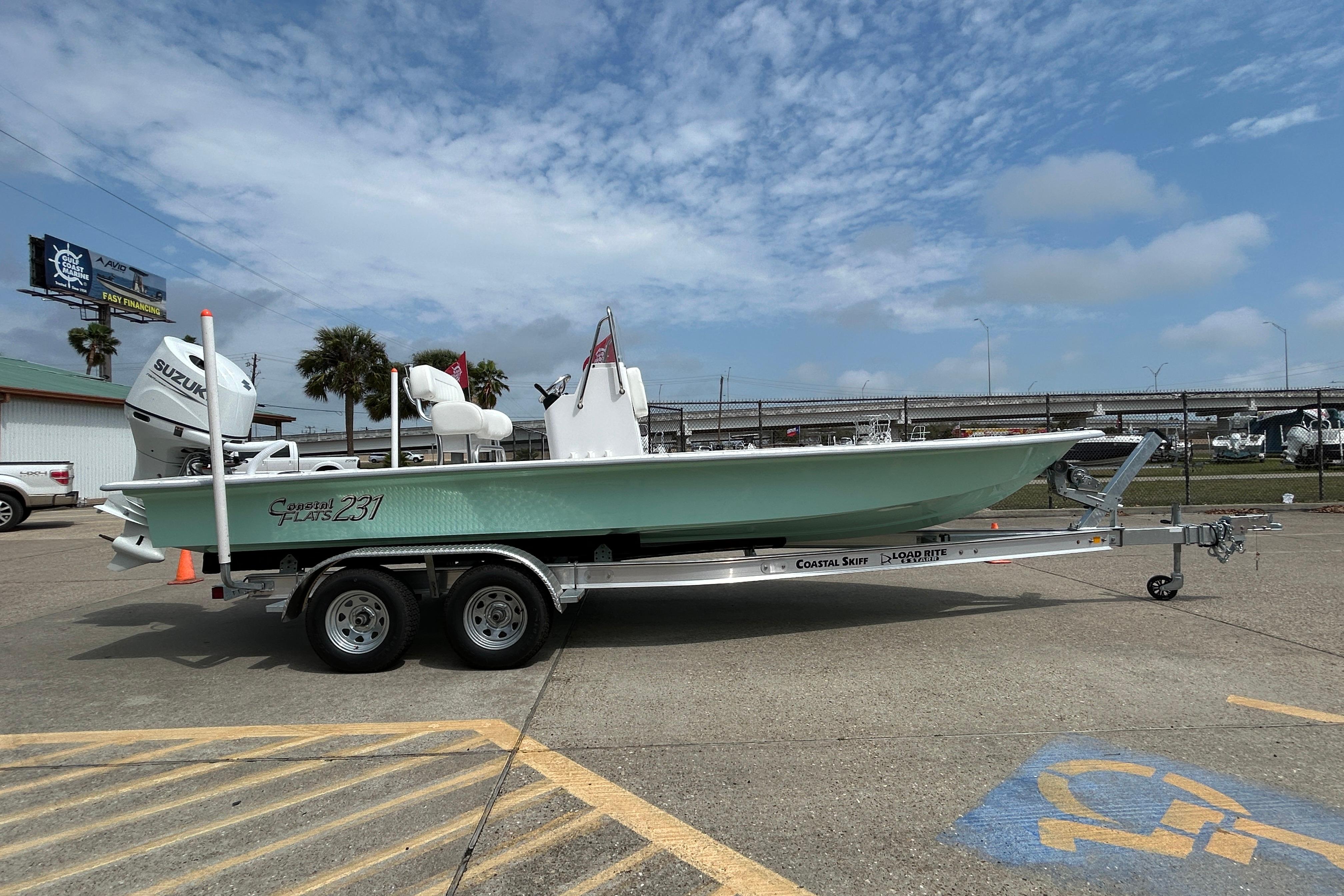 2026 Coastal Skiff 231 Flats boat on trailer, parked outdoors under a cloudy sky.