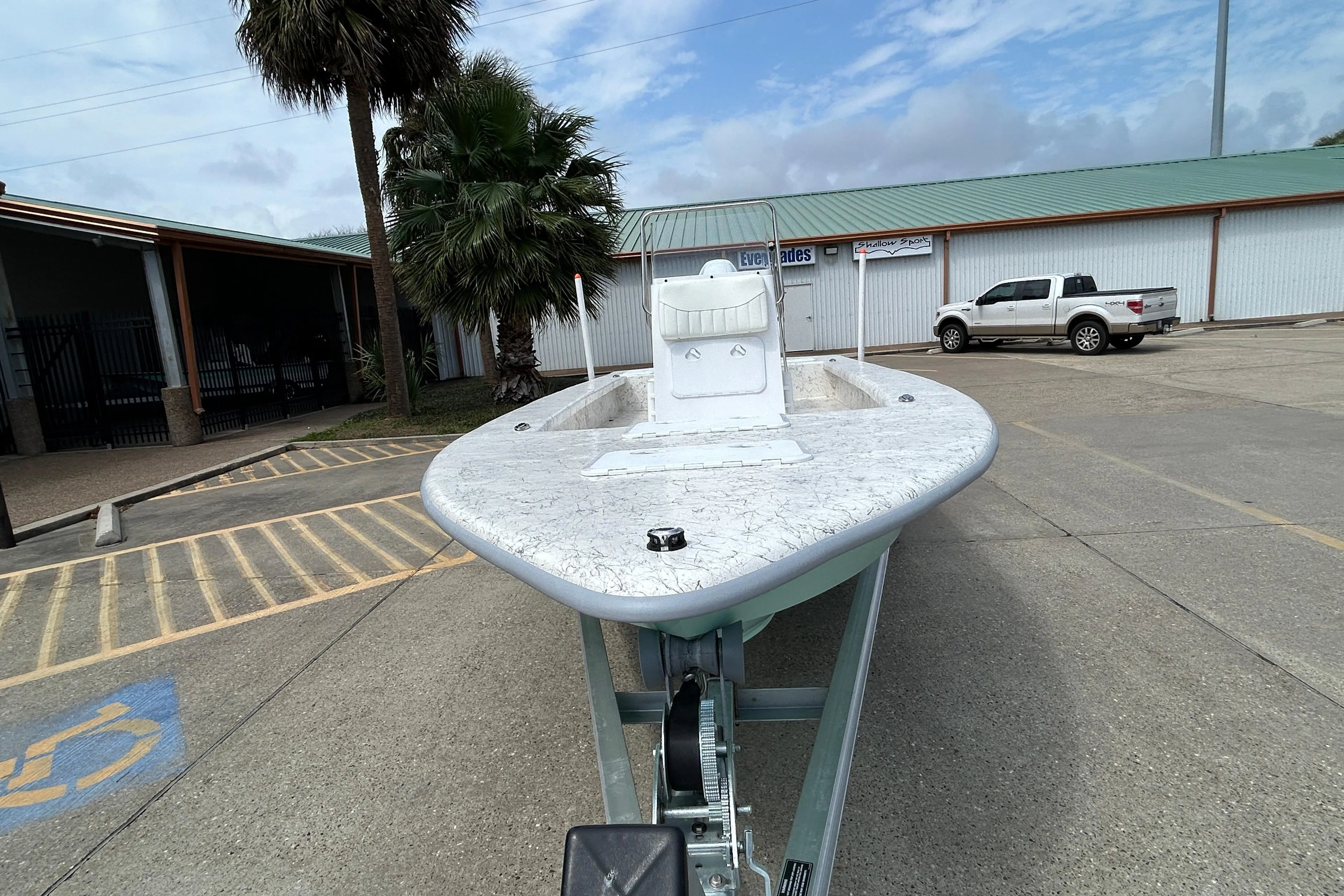 2026 Coastal Skiff 231 Flats boat on trailer in parking lot, palm tree nearby.