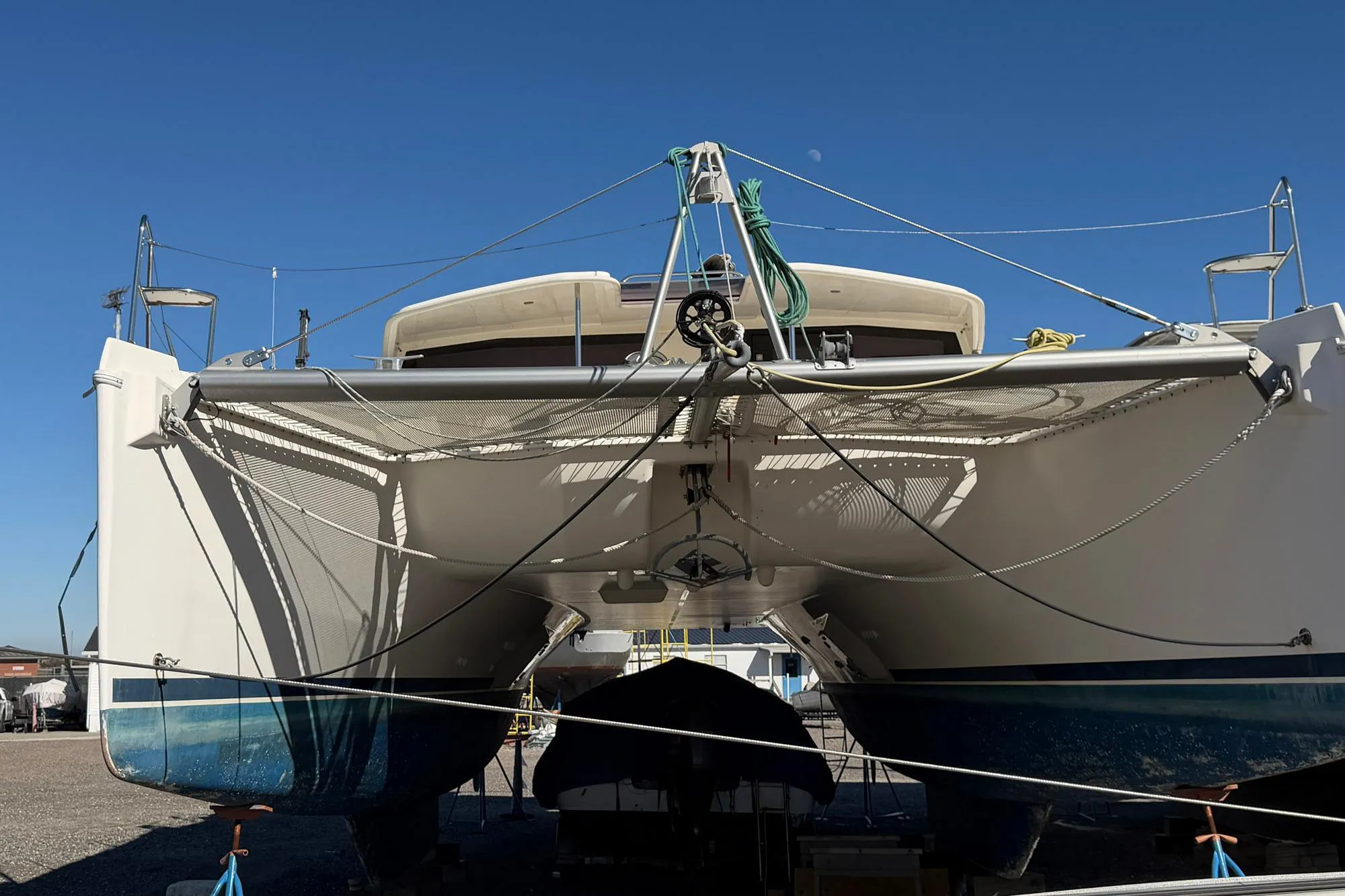 2015 Leopard 48 catamaran on land, showcasing hull and netting under clear blue sky.