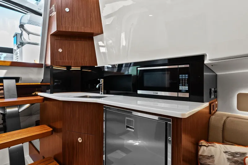  Yacht Photos Pics 2023 Sea Ray Sundancer 370 Outboard interior kitchen with microwave, sink, and wooden cabinetry.