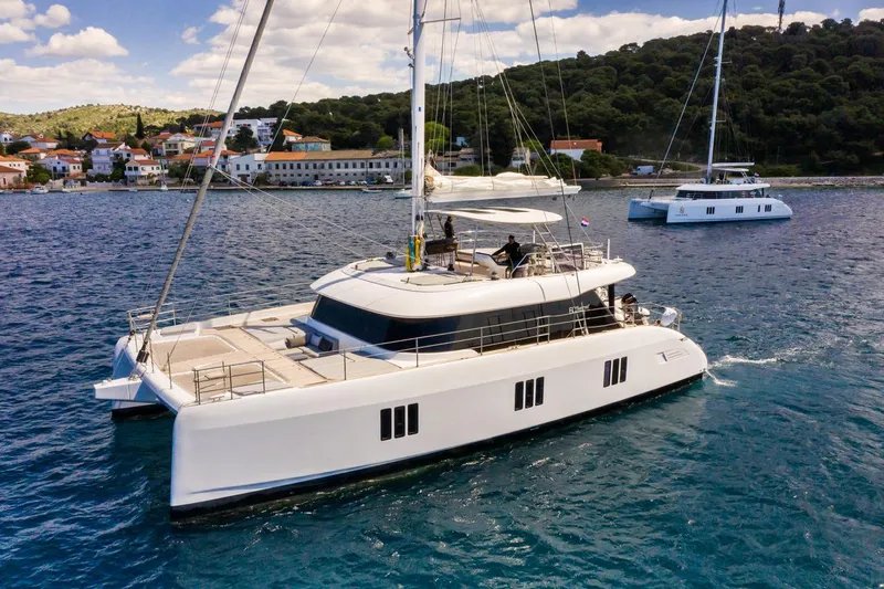Mr.si. Yacht Photos Pics Luxurious 2023 Sunreef 60 catamaran sailing near a coastal village.