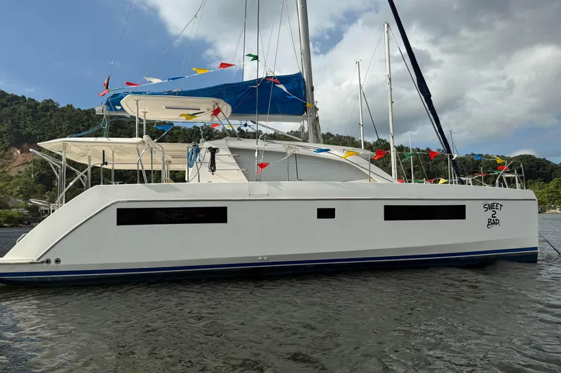 Sweet 2 Bad Yacht Photos Pics 2016 Leopard 404 catamaran with colorful flags, anchored near lush green hills.