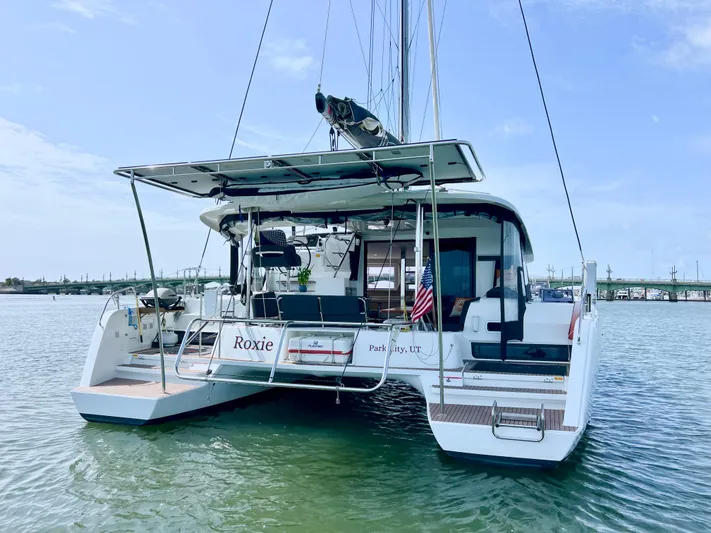 Roxie Yacht Photos Pics 2024 Lagoon 42 catamaran on water, rear view, with American flag and clear sky.