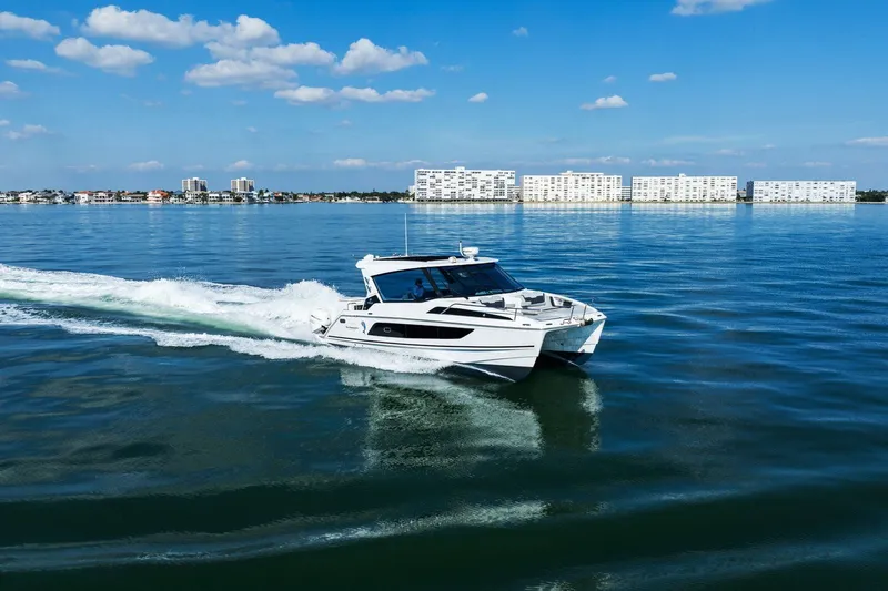  Yacht Photos Pics Aquila 36 boat cruising on calm waters, cityscape in background, clear blue sky.