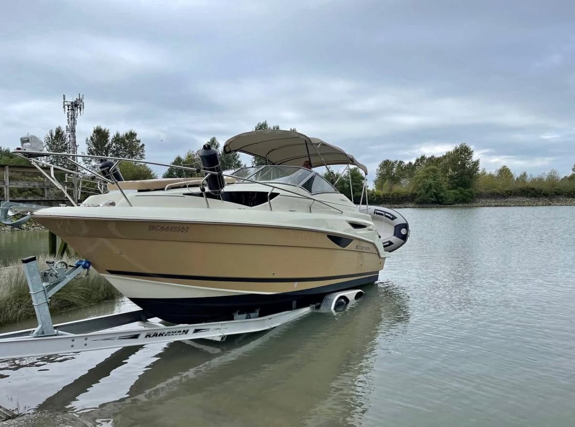 2014 Larson Cabrio 285 boat on trailer by a calm river under cloudy sky.