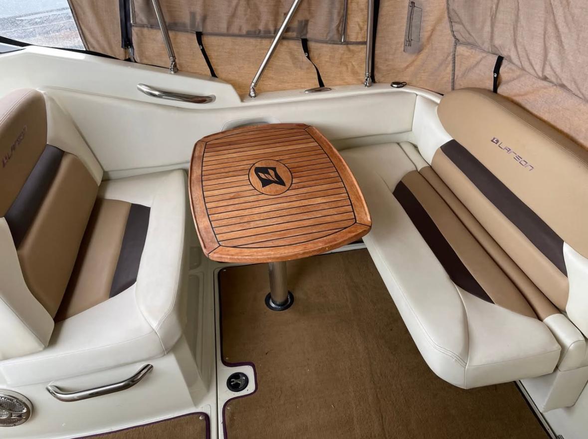 2014 Larson Cabrio 285 boat interior with cushioned seating and wooden table.