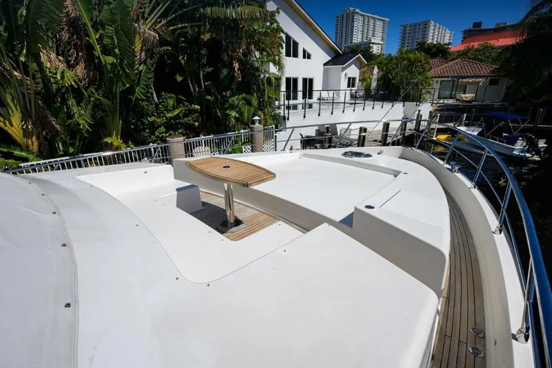  Yacht Photos Pics Front deck of a 2014 Hampton Fly yacht with a wooden table, docked near lush greenery.