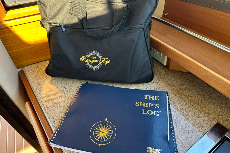 Two For The Road II Yacht Photos Pics Black Ranger Tugs bag and ship's logbook on a wooden boat interior surface.