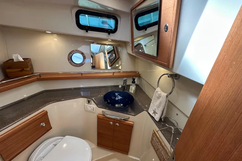 Two For The Road II Yacht Photos Pics 2020 Ranger Tugs R-29 bathroom with modern fixtures, wooden cabinetry, and a porthole window.