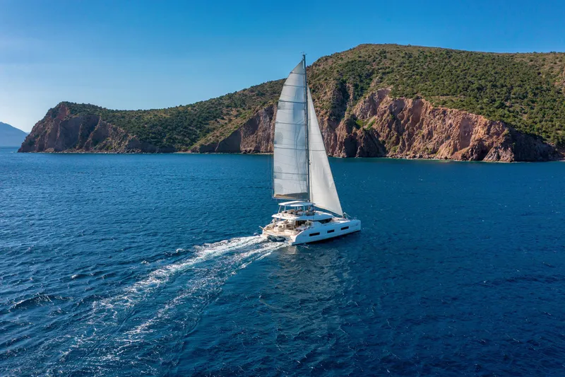  Yacht Photos Pics Sailing Lagoon 55 yacht, 2023 model, cruising in clear blue waters near rocky coastline.