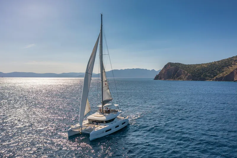  Yacht Photos Pics 2023 Lagoon 55 sailing in serene blue waters near rocky coastline.